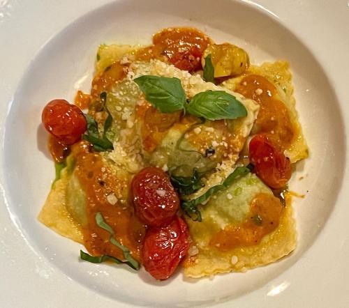 A plate of ravioli topped with cherry tomatoes, basil, and a rich tomato sauce, garnished with grated cheese.