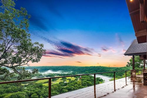 A scenic view from a balcony overlooking a misty valley and river at sunrise, with colorful clouds in the sky.
