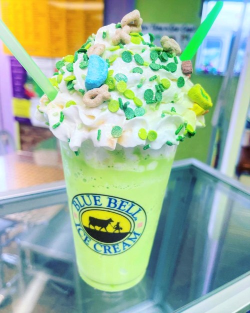 A vibrant green milkshake topped with whipped cream, colorful sprinkles, and candy, served in a Blue Bell Ice Cream cup.