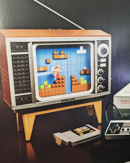 A retro-style TV made of LEGO displays a classic video game scene, with a game cartridge and controller nearby.