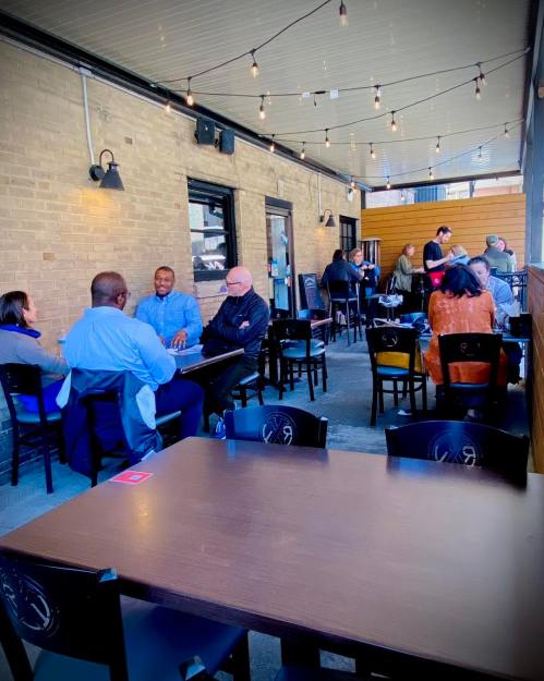 A lively outdoor dining area with people seated at tables, enjoying meals and conversation under string lights.