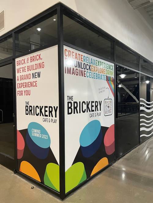 A colorful storefront sign for "The Brickery Café & Play," announcing a new experience coming summer 2023.
