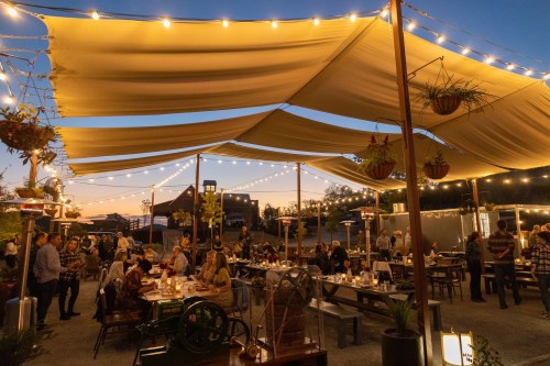Outdoor dining area with string lights, large canopies, and people enjoying a lively evening atmosphere.
