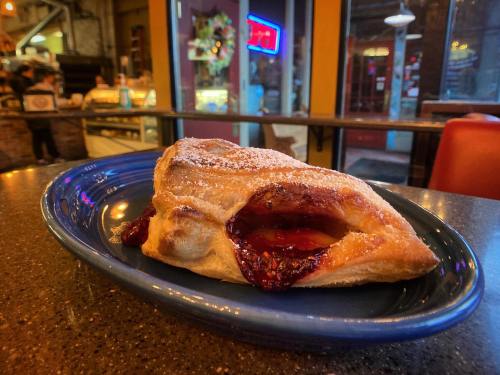 A flaky pastry filled with fruit jam, dusted with powdered sugar, served on a blue plate in a cozy café setting.