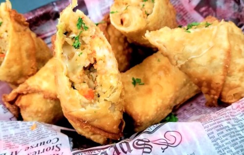 A close-up of crispy golden spring rolls filled with vegetables, garnished with parsley, served in a basket.