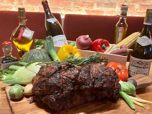 A beautifully arranged display of a roasted meat dish surrounded by fresh vegetables and bottles of wine.