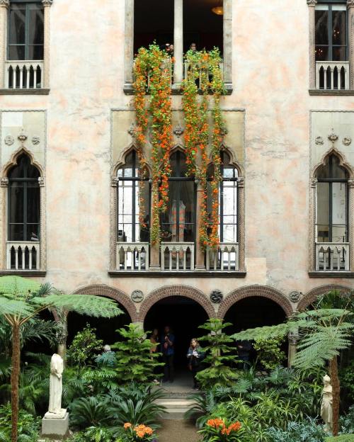 A lush courtyard with vibrant orange flowers cascading from windows, surrounded by greenery and architectural details.