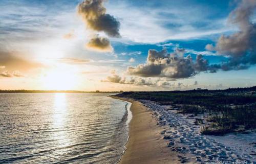 Sunset over a tranquil beach, with gentle waves lapping at the shore and clouds scattered in a blue sky.