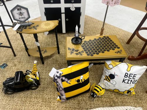 A display of bee-themed home decor, including tables, pillows, and a toy truck, all featuring yellow and black designs.