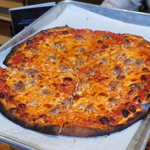 A freshly baked pizza with a golden crust, topped with melted cheese and chunks of sausage, on a baking tray.