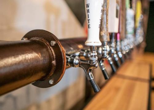 Close-up of a row of beer taps on a wooden bar, featuring various colorful tap handles.