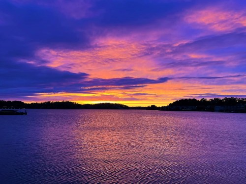A vibrant sunset over a calm lake, with purple and orange hues reflecting on the water's surface.