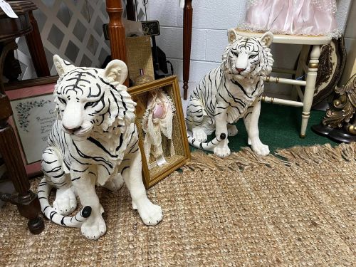 Two decorative white tiger statues with black stripes, positioned beside a framed picture and other vintage items.