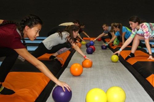 A group of children reaching for colorful dodgeballs on a trampoline court, focused and engaged in play.