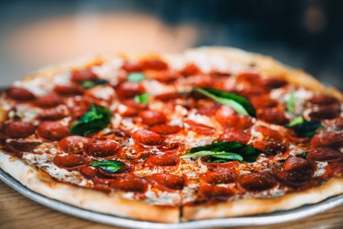 A close-up of a pepperoni pizza topped with fresh basil leaves on a silver platter.