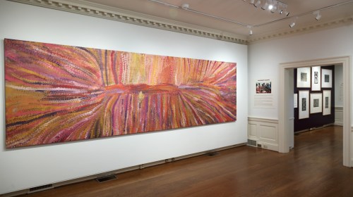A vibrant abstract painting with warm colors hangs on a gallery wall, showcasing dynamic brush strokes and textures.
