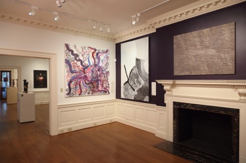 Art gallery interior featuring colorful abstract paintings and a minimalist artwork on the walls, with a fireplace.