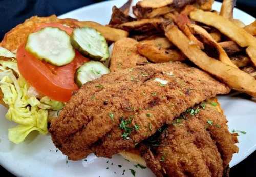 A plate featuring fried fish fillets, a sandwich with lettuce, tomato, pickles, and a side of crispy fries.