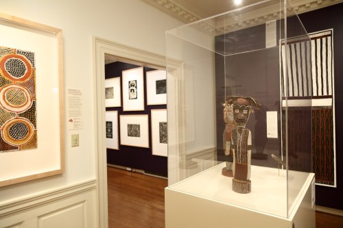 A gallery interior featuring a display case with an artifact and framed artworks on the walls.