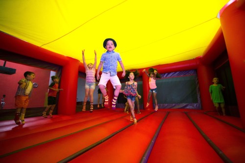Children joyfully jumping inside a colorful bounce house with a bright yellow ceiling and red walls.