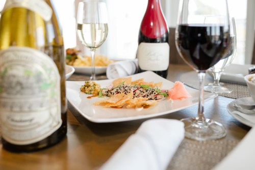 A beautifully plated dish with sushi, garnished with wasabi, alongside glasses of white and red wine.