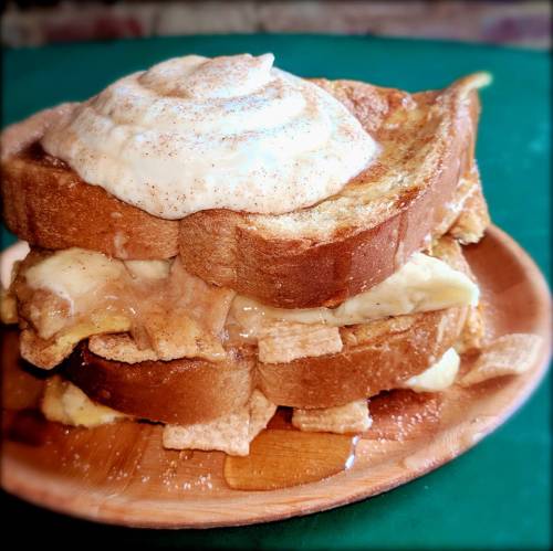 A stack of French toast topped with whipped cream and cinnamon, served on a wooden plate with syrup.