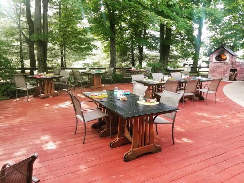 Outdoor dining area with wooden tables and chairs surrounded by trees, featuring a red wooden deck.
