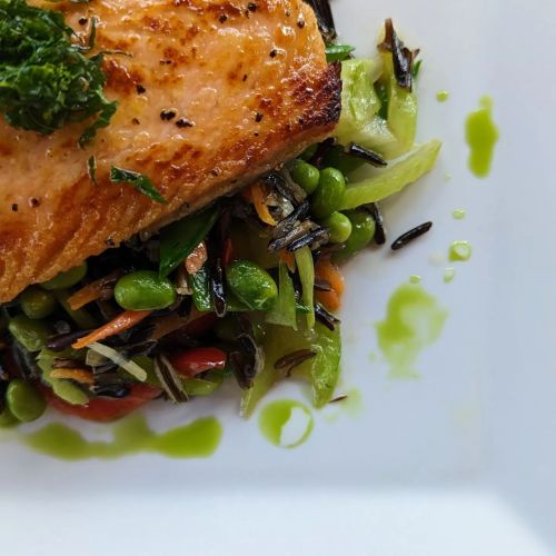 Grilled salmon fillet on a bed of colorful vegetables and wild rice, garnished with fresh herbs.