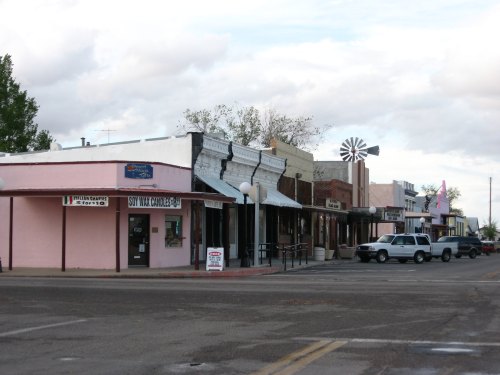 A quaint street lined with colorful storefronts and a windmill in the background under a cloudy sky.