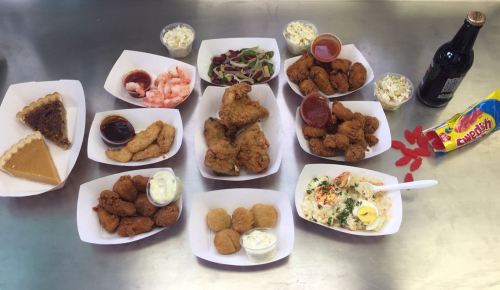 A variety of dishes including fried chicken, shrimp, coleslaw, desserts, and a drink arranged on a table.