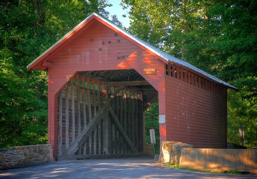 A red covered bridge surrounded by green trees, with a stone entrance and a clearance sign above.