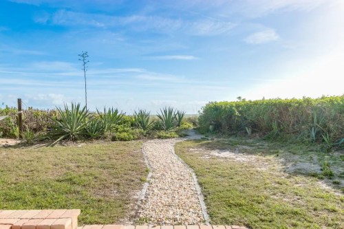 A winding stone path leads through lush greenery under a bright blue sky.
