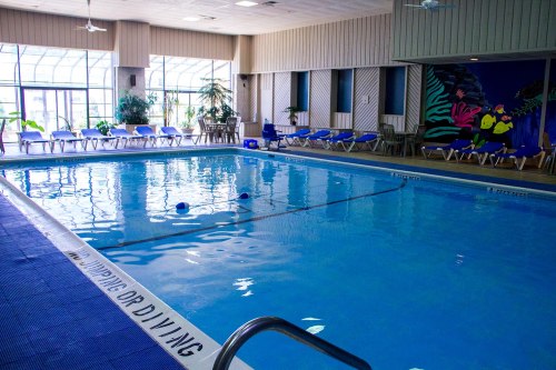 Indoor swimming pool with blue water, lounge chairs, and a colorful mural on the wall. Bright and inviting atmosphere.
