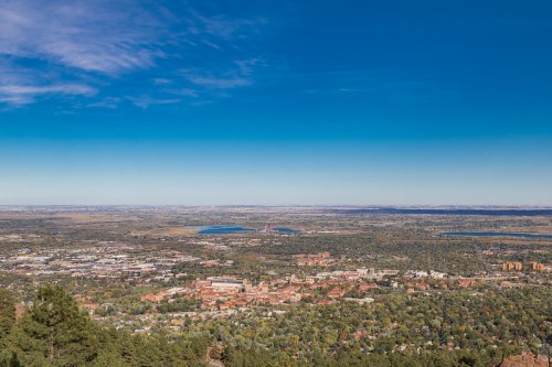 A panoramic view of a valley with greenery, buildings, and a clear blue sky in the background.