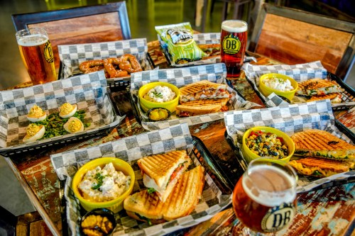 A table filled with various dishes, including sandwiches, pretzels, salads, and drinks, all served in baskets.