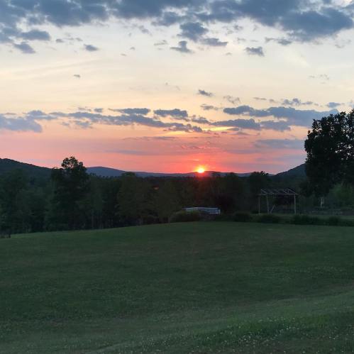 A serene sunset over rolling hills, with colorful clouds and a grassy foreground.