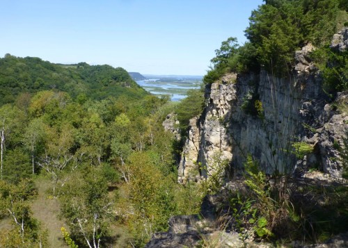 A scenic view of a river winding through lush green hills and rocky cliffs under a clear blue sky.