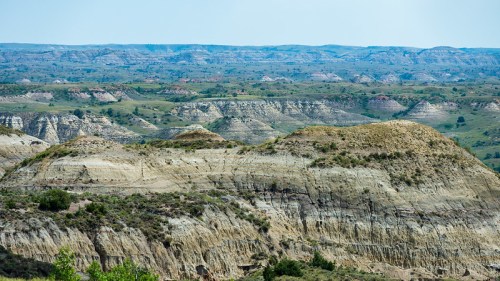 A panoramic view of layered hills and valleys in a rugged landscape under a clear blue sky.