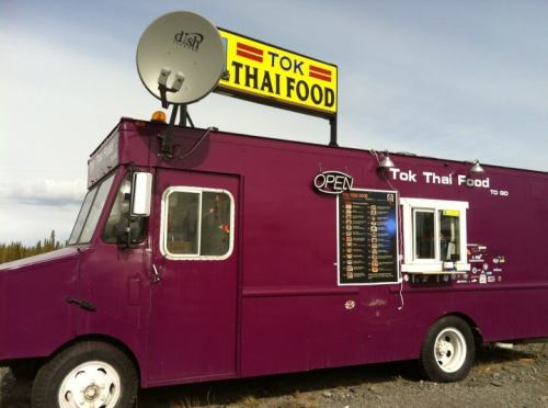 A purple food truck with a sign reading "Tok Thai Food" and an open window, parked in a rural area.