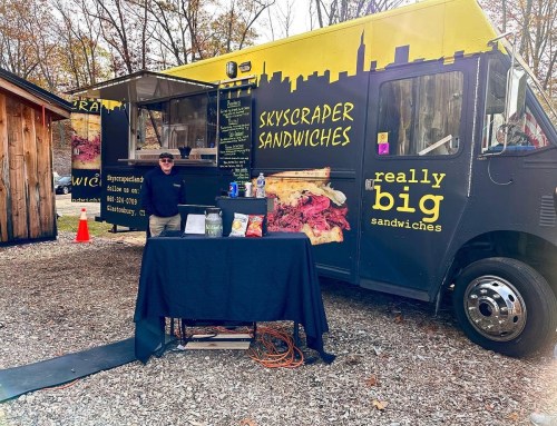 A food truck named "Skyscraper Sandwiches" with a vendor standing by a table in a wooded area.