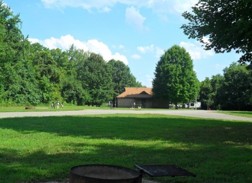 A grassy area with trees and a building in the background under a blue sky with scattered clouds.