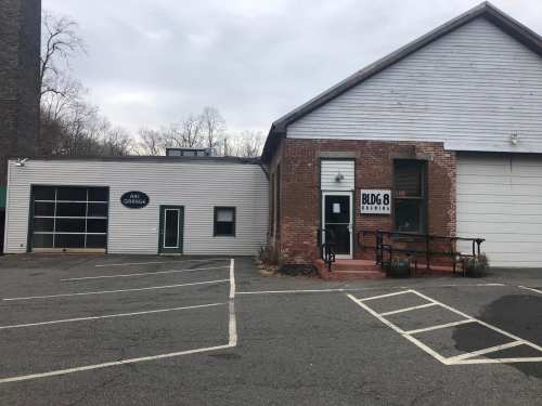 A building with a mix of brick and wood siding, featuring a garage door and a sign for "BUDG." Empty parking lot in front.