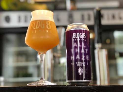 A glass of hazy beer next to a can from BLDG8 Brewing, showcasing a New England double IPA.