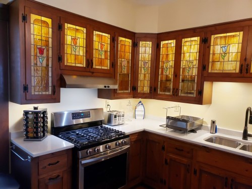 A cozy kitchen featuring stained glass cabinets, a stainless steel stove, and modern appliances on a white countertop.