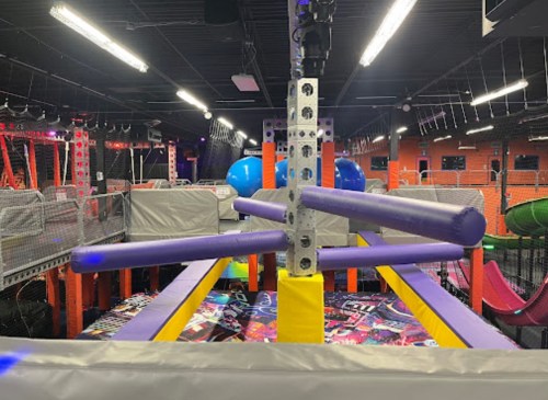 A colorful indoor trampoline park featuring various play structures and safety nets.
