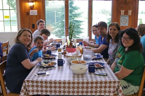 A group of people enjoying a meal together at a wooden table, with plates of food and drinks in a cozy setting.