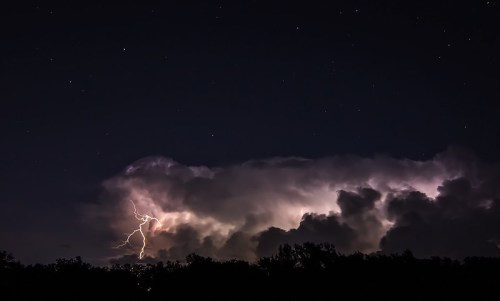A dramatic night sky with dark clouds illuminated by lightning, surrounded by twinkling stars.