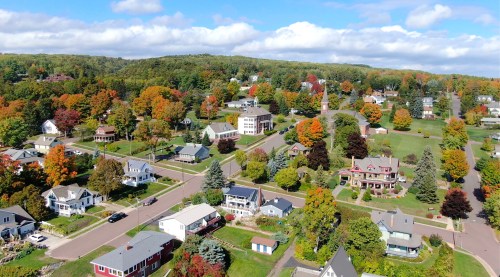Aerial view of a colorful autumn neighborhood with trees, houses, and a clear blue sky.