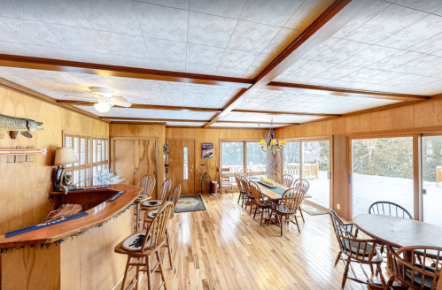 Cozy wooden dining area with a bar, large windows, and a view of snow-covered outdoors. Warm, inviting atmosphere.