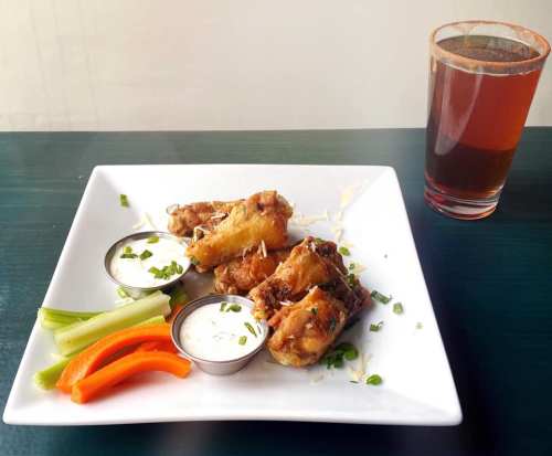 A plate of crispy chicken wings with dipping sauces, celery, and carrot sticks, alongside a glass of beverage.